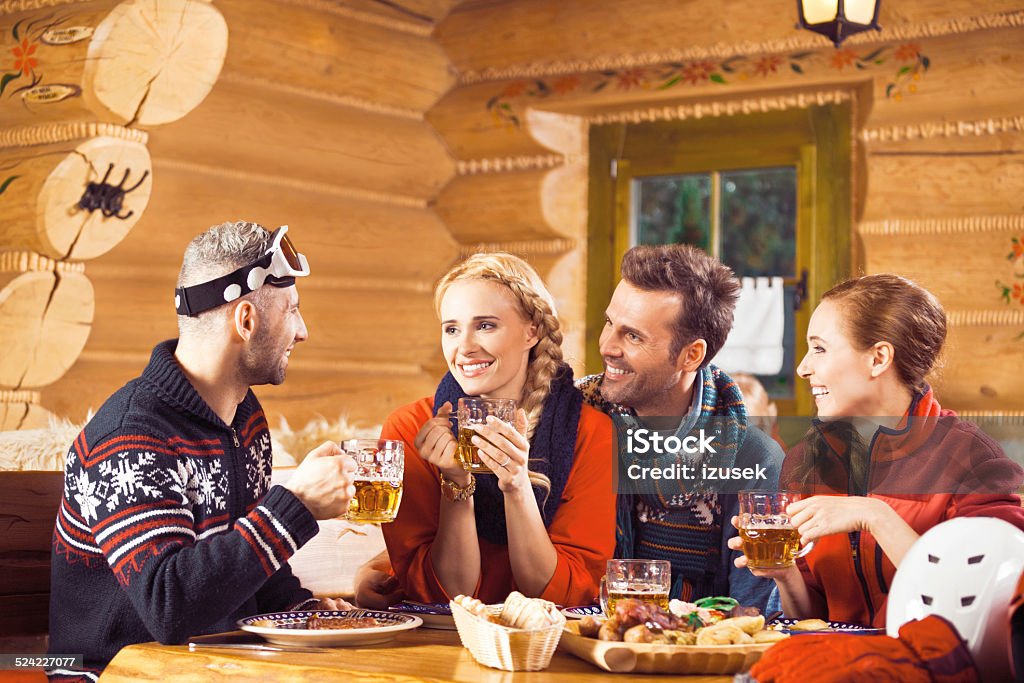 Friends having dinner in restaurant after skiing Two adult couples wearing winter clothes sitting in a mountain restaurant after skiing, having chat, enjoying dinner and drinking beer.  Apres-Ski Stock Photo