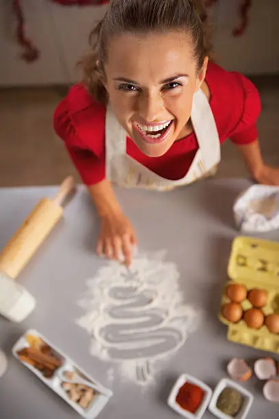 Photo of Smiling housewife drawing christmas tree on table with flour