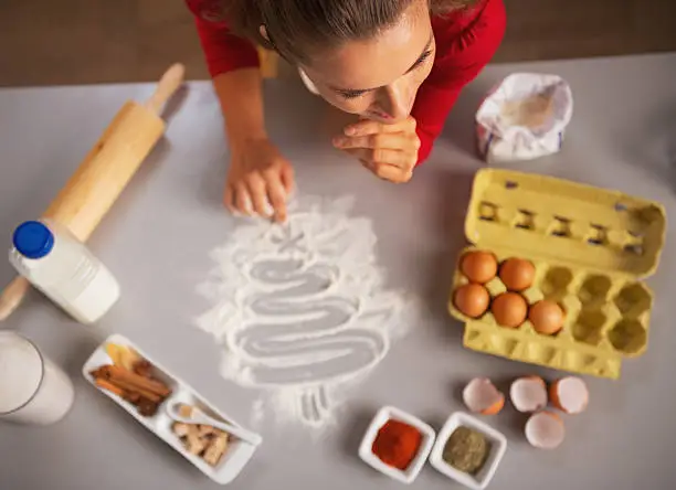 Photo of Housewife drawing christmas tree on kitchen table with flour