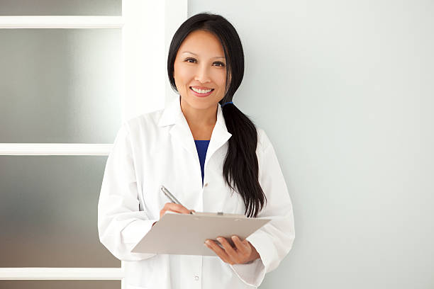 Confident Asian Woman Doctor Taking Notes On A Clipboard Confident Asian woman doctor taking notes on a clipboard when visiting a patient. This photo has been produced with professionals. laboratory coat stock pictures, royalty-free photos & images