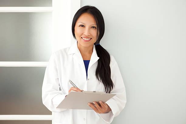 confiante asiática mulher médico tomar notas sobre uma prancheta - jaleco de laboratório - fotografias e filmes do acervo