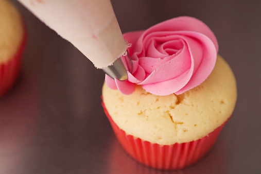 Close up pink rose frosted cupcake being iced Horizontal