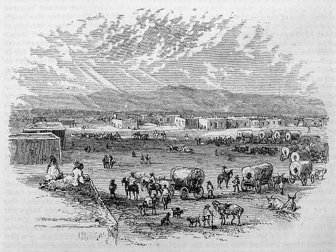 Several covered wagons bearing settlers from the east arrive in the adobe town of Conejos, Colorado.  Illustration from the May 1876 issue of Harper's New Monthly Magazine