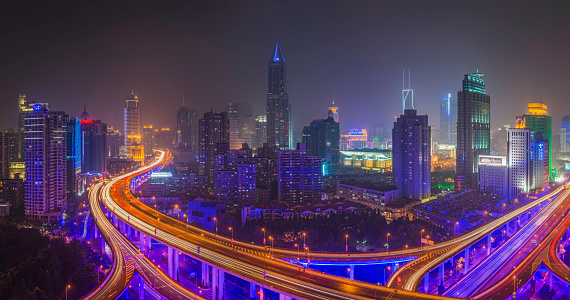 The futuristic neon lit highway and multi-layered Yan'an elevated interchange overlooked by the illuminated skyscrapers and dense housing of Shanghai's Huangpu district glowing in the vibrant city night. ProPhoto RGB profile for maximum color fidelity and gamut.
