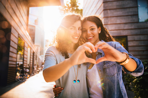 Best girl friends show heart shape to camera with hands