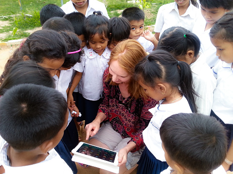 Siem Reap, Cambodia, - November 14,2014: European looking girl, showing how a tablet works to a group of school kids, near a village in Siem Reap.