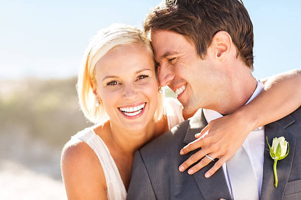 Bride Embracing Groom From Behind On Beach