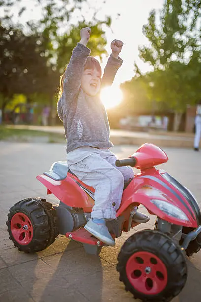 Photo of Cheerful little kid celebrating success on toy motorcycle.