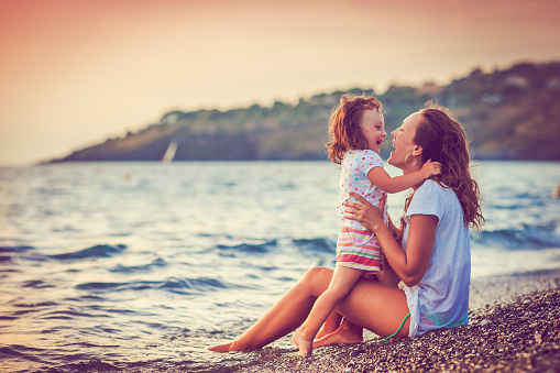 Happy little girl and her mother near the sea in sunset