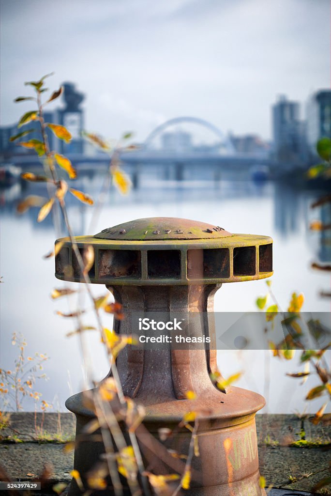 Derelict Graving Docks at Govan A rusting only iron capstan amongst the overgrowth at the derelict Victorian graving docks - a type of dry dock - in Govan, Glasgow, on the River Clyde. In the background is the modern Glasgow skyline. Govan Stock Photo