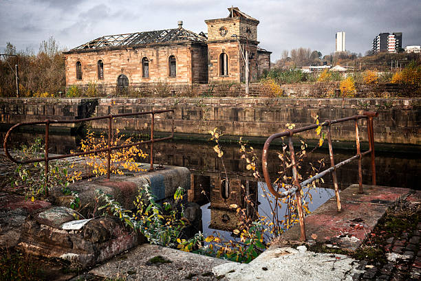 The Derelict Graving Docks at Govan, Glasgow Burnt out buildings amongst the overgrowth at the derelict Victorian graving docks - a type of dry dock - in Govan, Glasgow, on the River Clyde. In the background is the modern Glasgow skyline. govan stock pictures, royalty-free photos & images