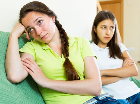 Two woman friends sitting on the coach discontent and having an argument