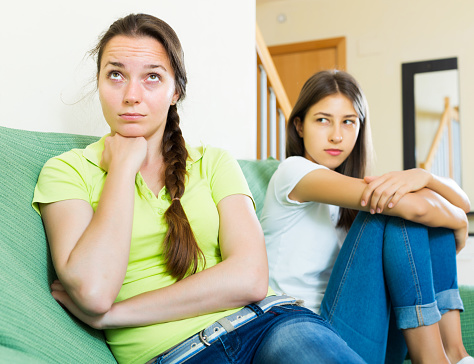 Two unhappy woman friends sitting on the coach discontent and having an argument