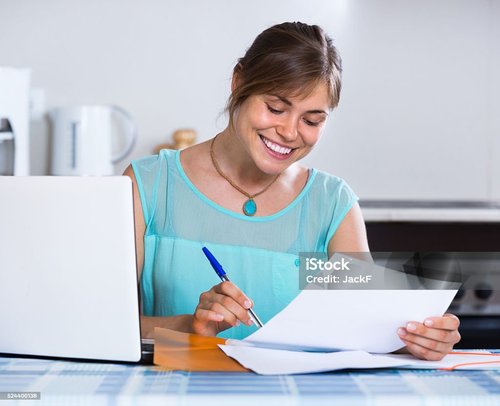 Smiling woman with documents at kitchen Young smiling brunette woman filling banking documents at the kitchen 25-29 Years Stock Photo