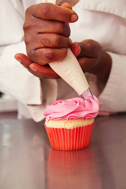 Pink rose icing being piped onto a cupcake vertical