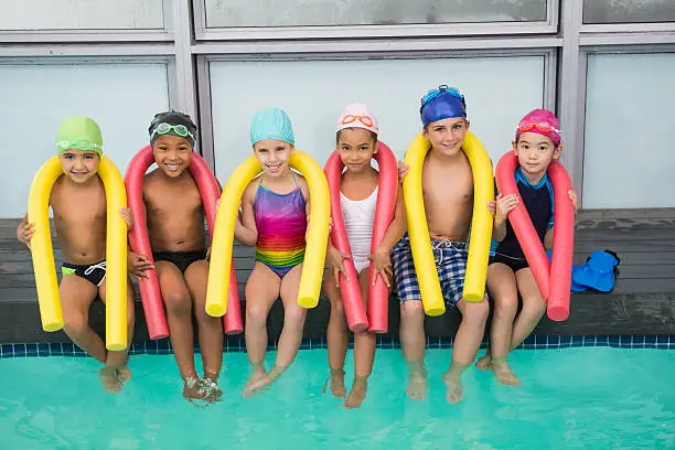 Cute swimming class smiling poolside at the leisure center