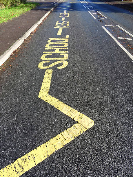 Yellow warning sign, School Keep Clear, painted tarmac road, no-parking