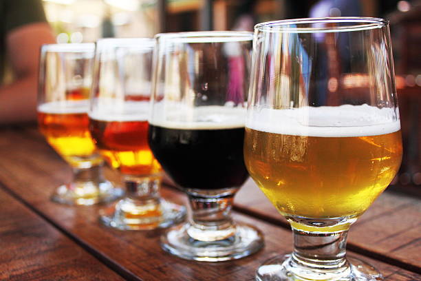 Beer Flight of four beers in glasses Flight of four beers lined up on a wooden table, with selective focus on the  first beer. Photo taken outdoors with natural lighting; beers range in color from light to very dark. Background out of focus. tasting stock pictures, royalty-free photos & images