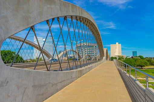 Bridge and walkway fills the foreground leading back to the skycrapers of Fort Worth skyline with clouds above, Texas