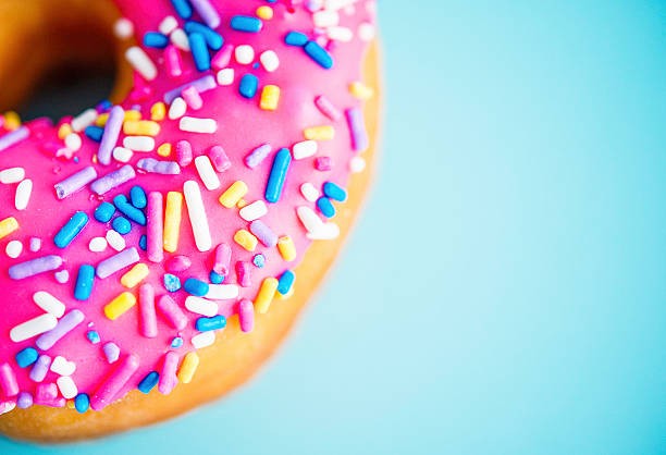 donut mit rosa zuckerguss und spritzer auf blauem hintergrund - sweet food sugar vibrant color multi colored stock-fotos und bilder