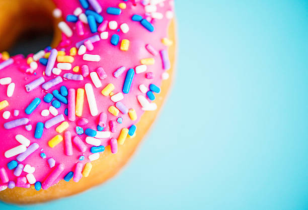 dónute com cobertura de rosa e sprinkles num fundo azul - sweet food sugar vibrant color multi colored imagens e fotografias de stock