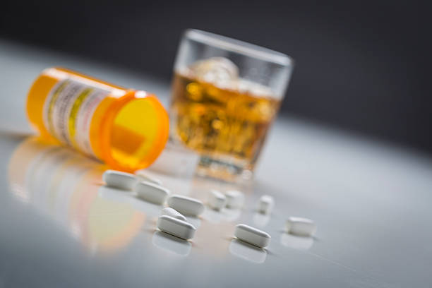 los medicamentos recetados vertido desde caído botella cerca de vaso de alcohol - bebida alcohólica fotografías e imágenes de stock