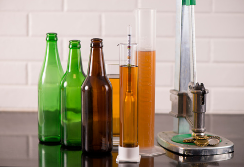 Making home brew process concept. Beer bottles, bottle capper, caps and test tube with hydrometer.