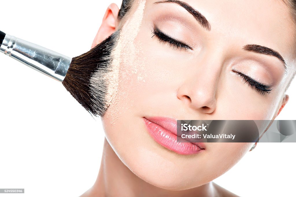 woman  applying dry cosmetic tonal foundation  on the face Closeup portrait of a woman  applying dry cosmetic tonal foundation  on the face using makeup brush.  Adult Stock Photo