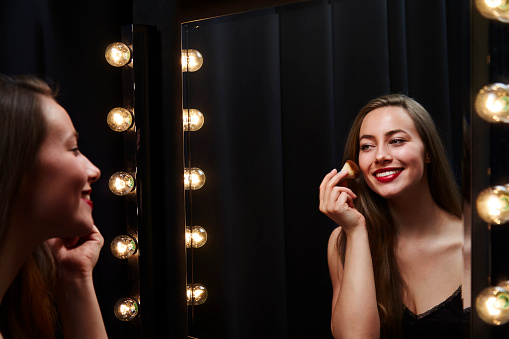 Young beautiful woman applying make up in mirror