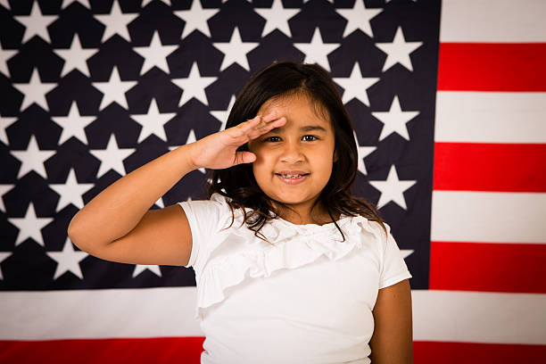 happy, young girl hacer un saludo en front of american flag - child patriotism saluting flag fotografías e imágenes de stock