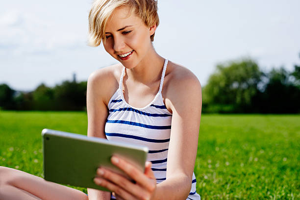 istock Young woman sitting on the grass and using a tablet 524582957