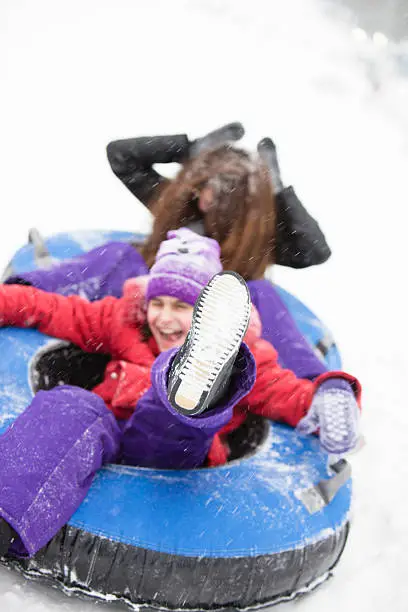 Two sisters, teenager girl and little girl, sliding at the slope and have fun with snowtubing at the winter resort 