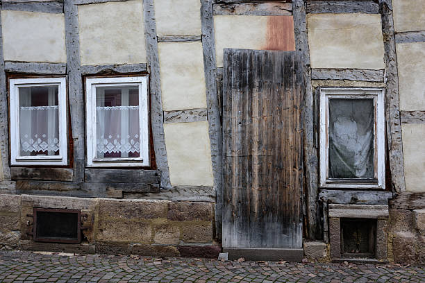 An old abandoned house with cracked plaster and exposed brick walls shows visible signs of decay and neglect. The roof with a small chimney and broken window adds to the impression of deterioration. The image reflects themes of aging, abandonment, and the passage of time.