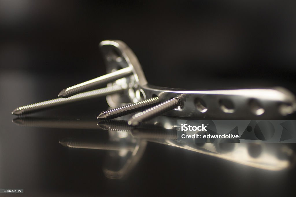 Traumatology orthopedic surgery implant plate and screws Traumatology orthopedic surgery implant titanium plate and silver color screws in semi silhouette against plain black studio background. Close-up macro horizontal photograph in grey tones with reflection.  Back Lit Stock Photo