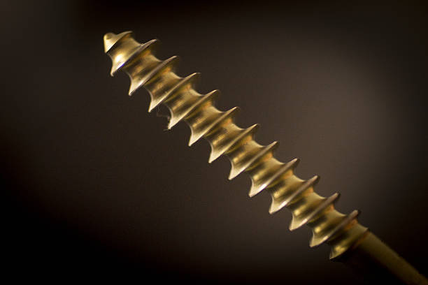 Traumatology orthopedic surgery implant screw Traumatology orthopedic surgery implant titanium golden color screw in semi silhouette against plain black studio background. Close-up macro horizontal photograph. tornillo stock pictures, royalty-free photos & images