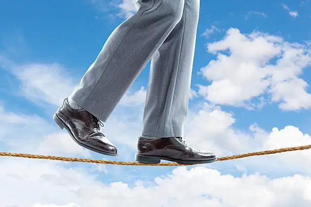 A businessman walking the tightrope balancing himself on white background.
