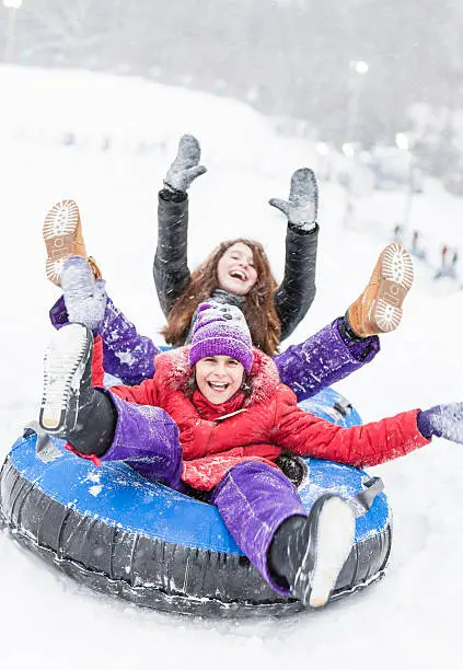 Two sisters, teenager girl and little girl, sliding at the slope and have fun with snowtubing at the winter resort 