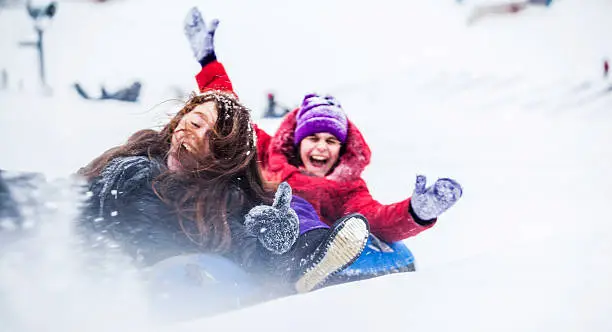 Two sisters, teenager girl and little girl, have fun with snowtubing at the winter resort 