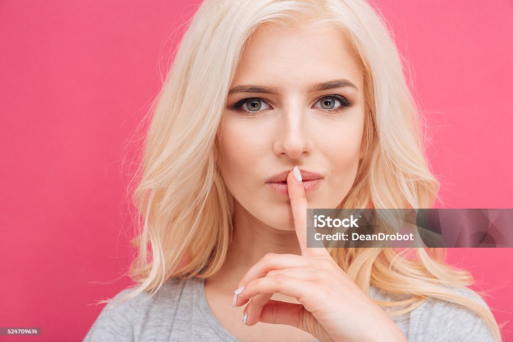 Pretty woman showing finger over lips Pretty woman showing finger over lips on pink background Adult Stock Photo