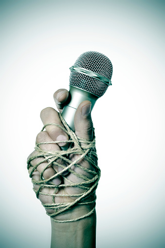 closeup of a microphone in the hand of a young man tied with rope, depicting the idea of the repression of the mass media or the lack of the freedom of speech