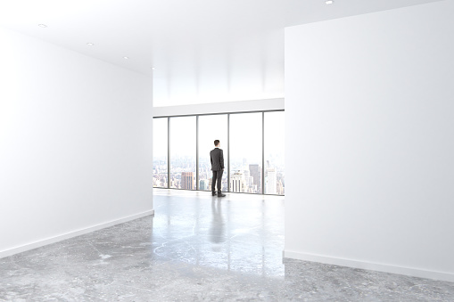 Businessman looking out the window in empty office with concrete floor and blank walls, mock up, 3D Render