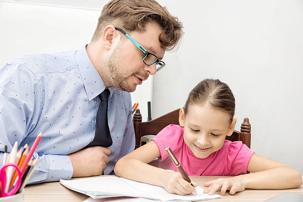 teacher and schoolgirl, father and daughter writing in classroom stock photo