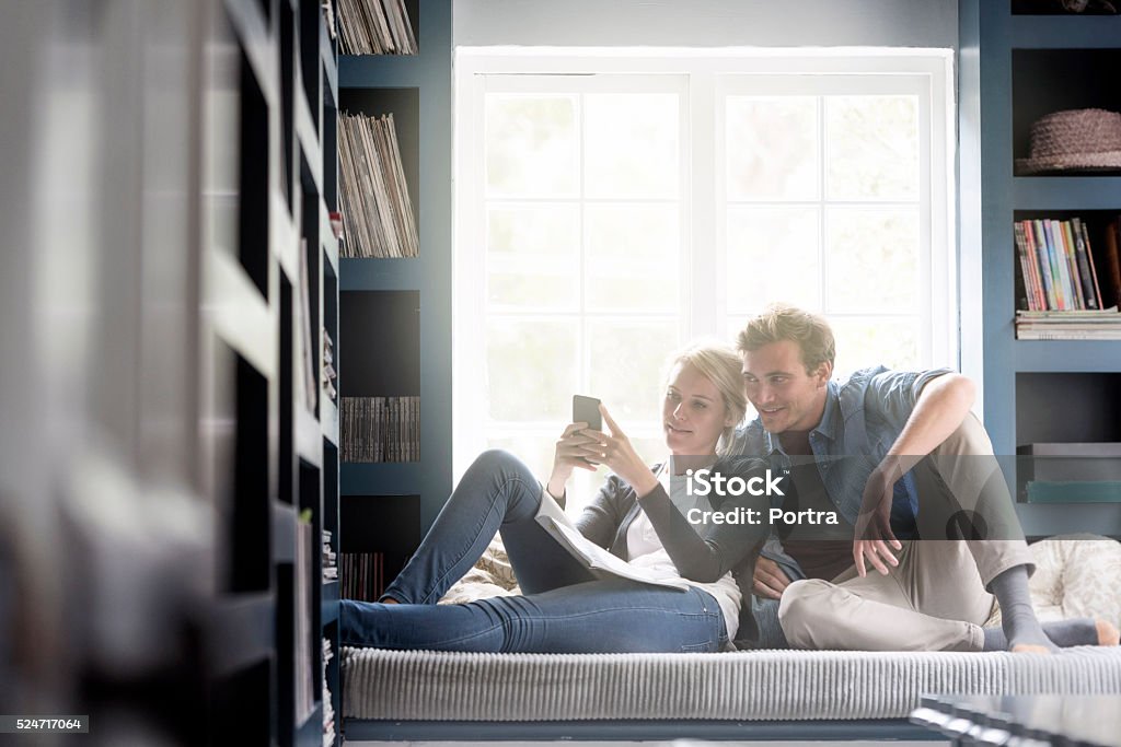 Jeune couple à l'aide de téléphone portable à la maison contre la fenêtre - Photo de Fenêtre libre de droits