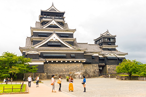 Kumamoto, Japan - August 10, 2014: Kumamoto Castle against bright sky, small group of japan tourist walking in front of it and two man dressed in samurai costume acting for the visitors.
