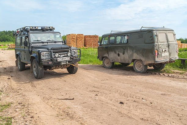 Land Rover Defender and UAZ-452 van stand on dirt road Kvazenga, Russia - June 23, 2010: All-terrain 4x4 Land Rover Defender SVX 60-year special edition vehicle and UAZ-452 (Bread loaf) unique off-road van stand on dirt road before board stack. uaz 4x4 land vehicle woods stock pictures, royalty-free photos & images
