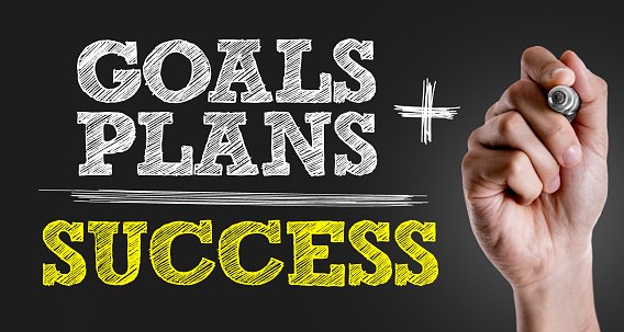 Hand writing the text: Goals + Plans = Success