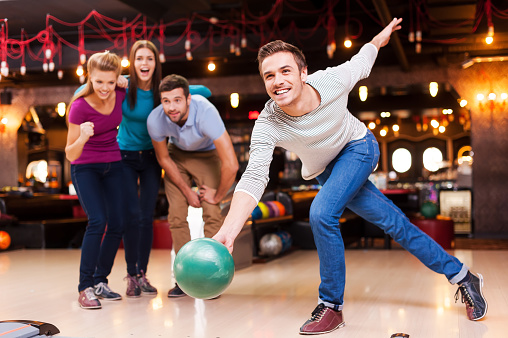 Handsome young men throwing a bowling ball while three people cheering