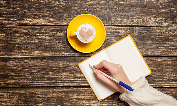 istock Female hand writing something in notebook near cup of coffee. 524817569