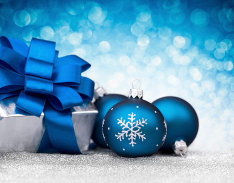 Three blue bauble and christmas gift on glitter.Silver gift with blue ribbon bow. One bauble decorated with snowflakes. Defocused light blue background. Shot with Nikon D800