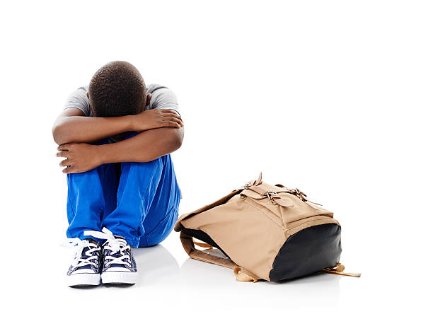 I don't want to Studio shot of a little boy with his head buried in his knees sitting next to his schoolbag against a white background sitting knees up stock pictures, royalty-free photos & images